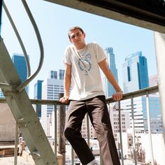 a young man standing on top of a metal rail next to a stair case in front of a cityscape