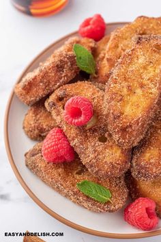 some fried french toast on a plate with raspberries and mint leaves around it