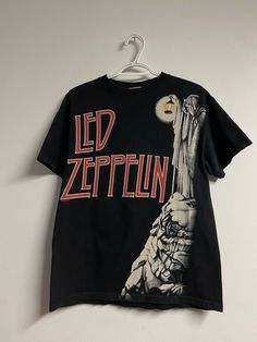 This Liquid Blue vintage T-shirt is a must-have for any Led Zeppelin fan. Featuring the iconic album artwork of "Hermit Stairway" on the front, this black tee is made of high-quality materials Size Medium Chest: 19.5" Length : 25" Hem: 20" Sleeve length: 5" No condition issues Music Festival Graphic Print Short Sleeve T-shirt, Band Logo Graphic Tee With Crew Neck, Graphic Tee With Band Logo And Crew Neck, Band Logo T-shirt, Crew Neck, Fan Merchandise, Band Logo T-shirt Fan Merchandise Crew Neck, Band Merch T-shirt With Graphic Print For Fans, Band Merch Graphic Print T-shirt For Fans, Pop Culture Crew Neck T-shirt With Band Logo, Band Merch T-shirt With Graphic Print