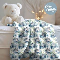 a white teddy bear sitting on top of a bed next to a blue and white blanket