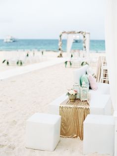 an outdoor wedding setup on the beach with gold and white linens, flowers and decorations