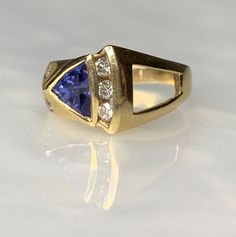 Tanzanite Ring, Trillion Cut Ring, Tanzanite Engagement Ring, Trillion Tanzanite Ring, Geometric Gemstone Ring, Gemstone Engagement Ring A fascinating and shapely vintage tanzanite ring boasting a 1.53 carat trillion cut tanzanite uniquely set on an angle surrounded by sparkling white diamonds weighing 0.48 carats set in solid 14k yellow gold with a modern asymmetric design. *Ring size: US 6 3/4 *Ring weight: 6.54 grams *Complimentary resizing is available up to 3 sizes larger or smaller than st Trillion Cut Diamond Ring With Gemstone For Formal Occasions, Formal Trillion Cut Diamond Ring With Gemstone, Formal Rings With Trillion Cut Center Stone, Fine Jewelry Trillion Cut Sapphire Ring With Accent Stones, Sapphire Gemstone Ring, Trillion Cut, Trillion Cut Sapphire Gemstone Ring, Formal Rings With Accent Stones In Trillion Cut, Formal Ring With Trillion Cut And Accent Stones, Fine Jewelry Multi-stone Trillion Cut Ring