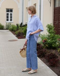 a woman is standing on the sidewalk with her hand in her pocket and holding a purse