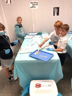 three children are standing around a table with blue cloths on it and masks covering their faces