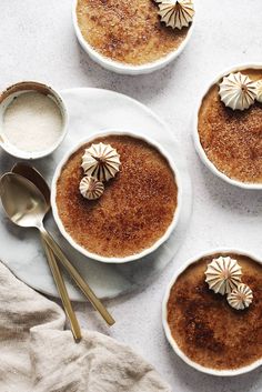 three bowls filled with dessert sitting on top of a white table next to spoons