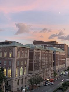 the sun is setting over an old building and cars are parked on the side of the road