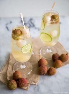 two glasses filled with drinks sitting on top of a table next to kiwis