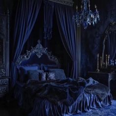 a bed with blue sheets and curtains in a dark room next to a chandelier