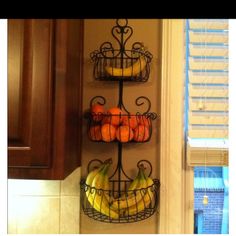 two metal baskets filled with fruit on top of a kitchen counter next to a window