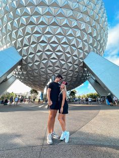 a man and woman standing in front of the spaceship building at disney world with their backs to each other