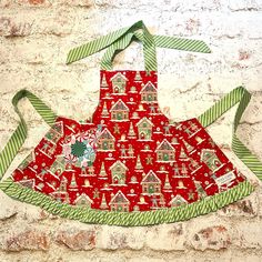 an apron hanging on a brick wall with green and red trimmings, decorated with gingerbread houses