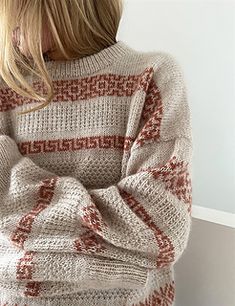 a woman standing in front of a white wall wearing a sweater with red and beige stripes