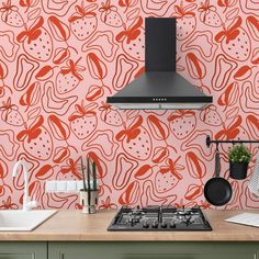 an orange and red wallpaper in a kitchen with stove top hood over the range