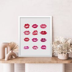 a white framed print with pink and red lipstick prints on it next to vases