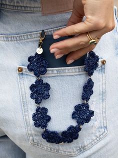 a woman's hand holding onto a cell phone in her jeans pocket with a crocheted necklace on it