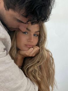 a man and woman embracing each other in front of a white wall with long hair