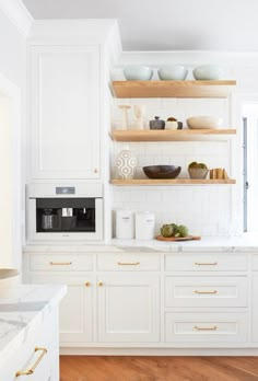 a white kitchen with open shelving and wooden shelves on the wall next to an oven