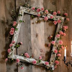 an old wooden frame with pink flowers on it and a candle in front of it