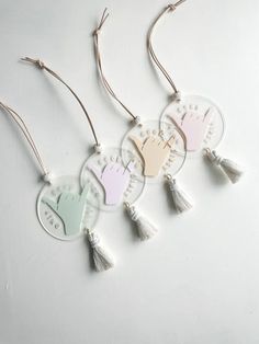 three ornaments with hand prints and tassels hanging from strings on a white surface