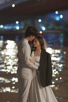 a man and woman standing next to each other in front of the water at night