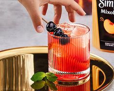 a hand reaching for an alcoholic drink in a glass on a gold tray next to a bottle