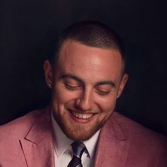 a man in a pink suit smiling and looking down at his cell phone while wearing a tie