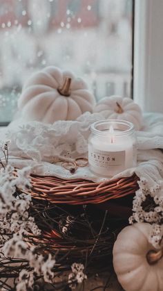 a white candle sitting on top of a wicker basket next to some pumpkins