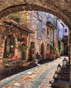 an alley way with tables and chairs on the side, surrounded by stone buildings in italy