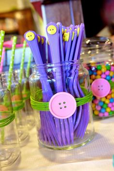 purple and green plastic straws with buttons on them are sitting in a glass jar