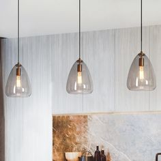 three clear glass pendant lights hanging from the ceiling above a kitchen counter with utensils on it