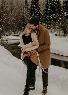 a man and woman standing in the snow next to each other with their arms around each other