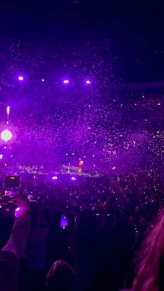 a large crowd at a concert with confetti falling from the ceiling and people taking pictures on their cell phones