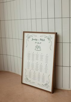 a wedding seating chart in front of a white tiled wall with brown frame on it