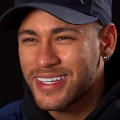 a close up of a person wearing a baseball cap and smiling at the camera with a black background