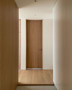 an empty hallway with wooden doors leading to another room that has white walls and wood flooring