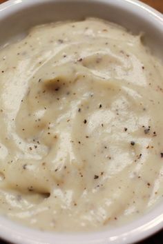 a white bowl filled with cream sauce on top of a wooden table next to a spoon