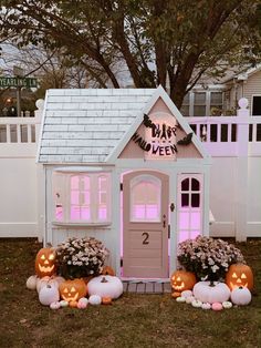 a small white house with pumpkins and flowers in the front yard for halloween decorations