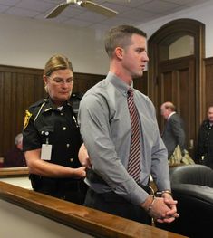 two men in suits and ties are standing at a courtroom table with other people behind them