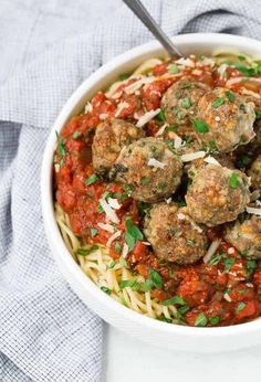 a white bowl filled with meatballs and pasta on top of a blue towel next to a fork