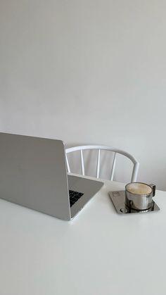 an open laptop computer sitting on top of a white table next to a cup of coffee