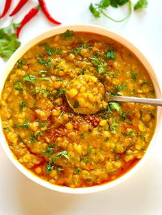 a white bowl filled with soup and garnished with cilantro, parsley and red peppers