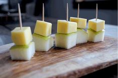 several cubes of cheese are on a wooden cutting board with toothpicks sticking out of them