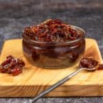 a wooden cutting board topped with a bowl filled with raisins next to two spoons