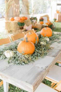 a table with pumpkins and greenery is set up for an outdoor wedding reception