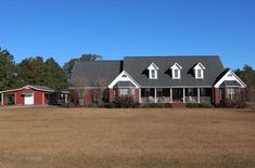 a red and white house sitting in the middle of a field with two garages