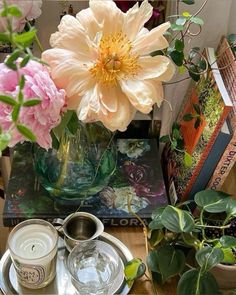 a table topped with flowers and books next to a vase filled with pink peonies