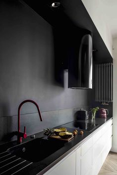 a kitchen with black walls and white cupboards, an island sink and red faucet