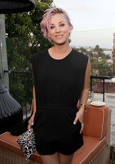 a woman with pink hair and black dress posing for the camera on a patio area