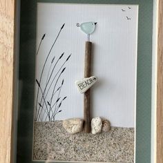 there is a picture frame with a bird on the branch and rocks in the sand