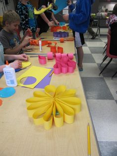 several children are sitting at a table making crafts with construction paper and colored pencils